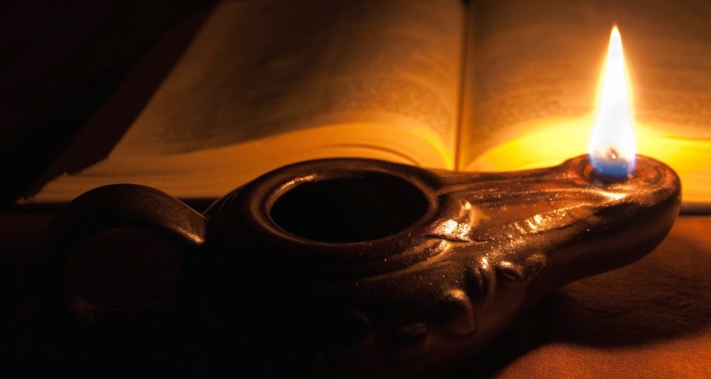 a clay lamp with a burning wick illuminates an open bible